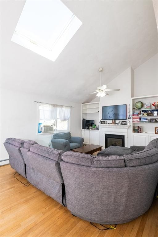 living area featuring ceiling fan, a glass covered fireplace, lofted ceiling with skylight, and light wood-style floors