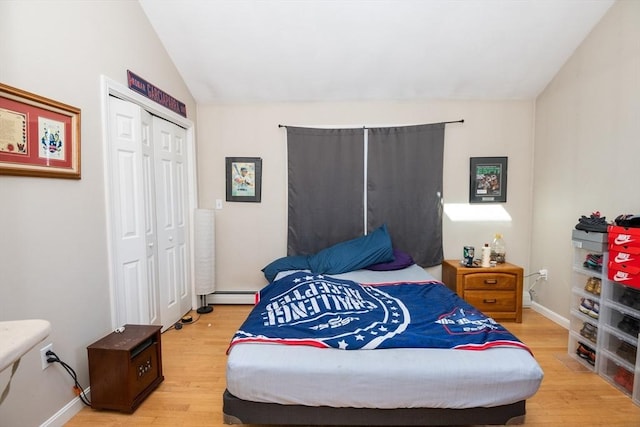 bedroom with baseboard heating, vaulted ceiling, baseboards, a closet, and light wood finished floors