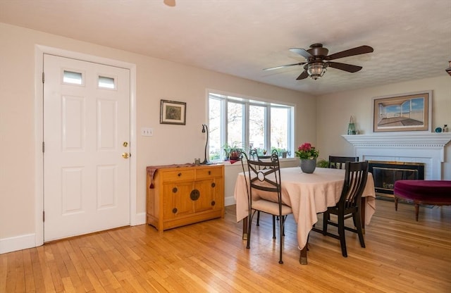 dining area with baseboards, a brick fireplace, light wood finished floors, and ceiling fan