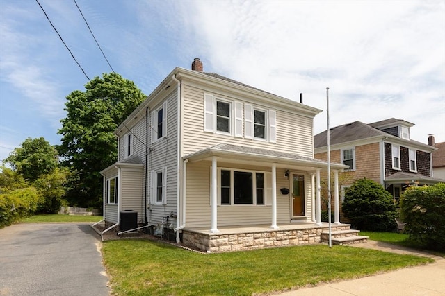 american foursquare style home with covered porch, a chimney, a front yard, asphalt driveway, and central AC unit