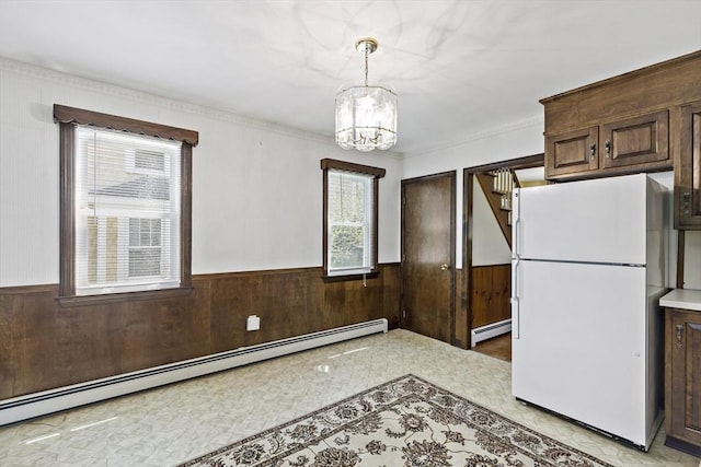 kitchen with freestanding refrigerator, baseboard heating, a wainscoted wall, a chandelier, and wooden walls