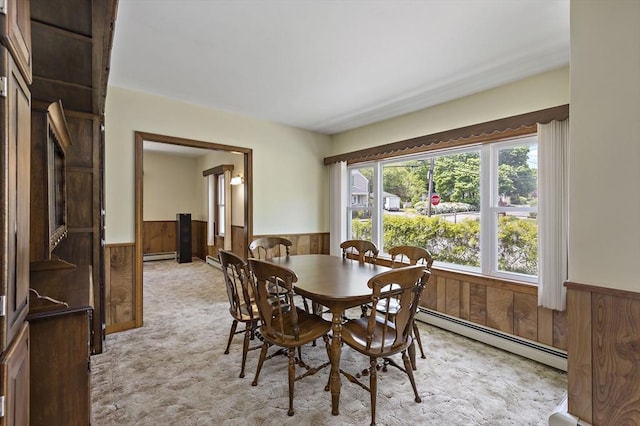 dining room featuring wainscoting, a baseboard radiator, wooden walls, and light carpet