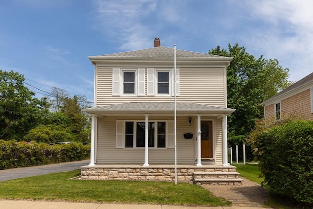 view of front of home with covered porch, a chimney, roof with shingles, and a front lawn