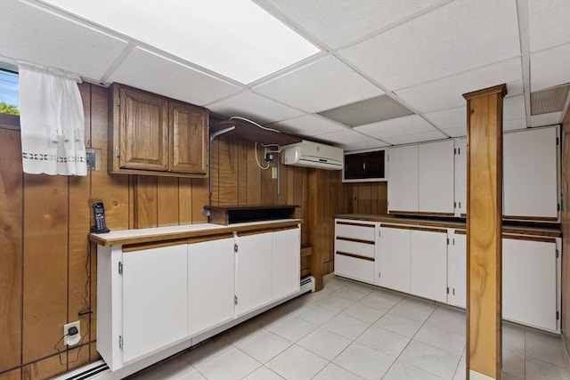 kitchen featuring an AC wall unit, wood walls, a drop ceiling, light tile patterned floors, and white cabinetry