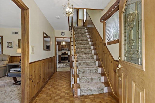 entrance foyer featuring wooden walls, stairs, a wainscoted wall, and a chandelier