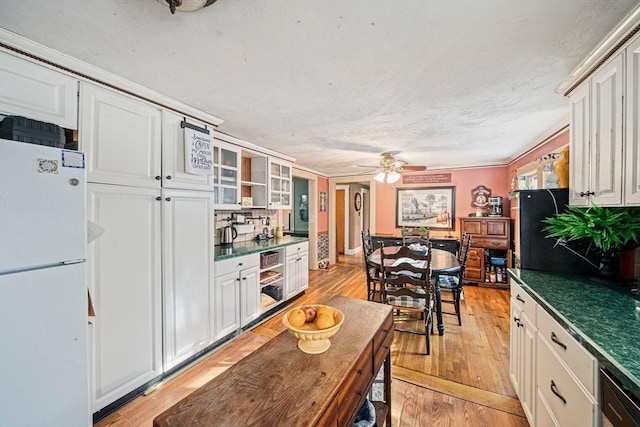 kitchen with dark countertops, freestanding refrigerator, a ceiling fan, and light wood-type flooring