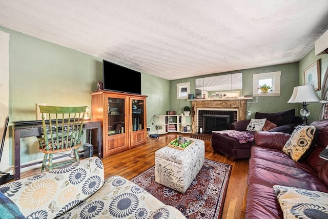 living room with a brick fireplace, a textured ceiling, and wood finished floors