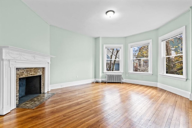 unfurnished living room featuring radiator heating unit, light hardwood / wood-style floors, and a brick fireplace