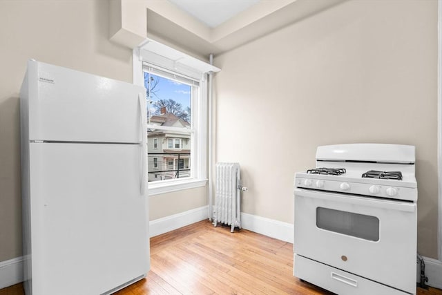 kitchen featuring radiator heating unit, white appliances, light hardwood / wood-style flooring, and a healthy amount of sunlight