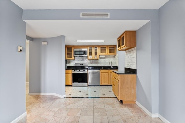 kitchen featuring stainless steel appliances, tasteful backsplash, visible vents, glass insert cabinets, and dark countertops