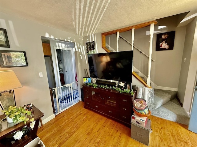 living room featuring stairs, wood finished floors, a textured ceiling, and baseboards