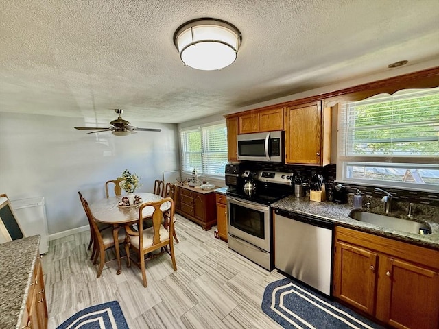 kitchen featuring appliances with stainless steel finishes, a sink, a textured ceiling, brown cabinetry, and ceiling fan