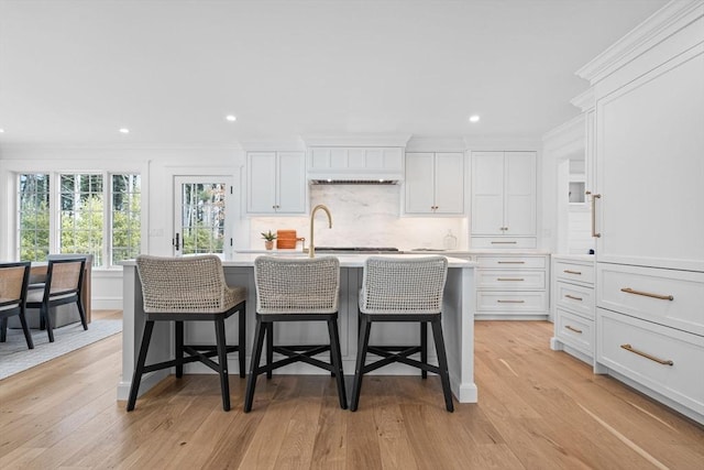 kitchen featuring a kitchen island with sink, light wood-type flooring, light countertops, and ornamental molding