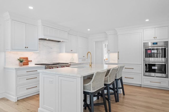 kitchen featuring a sink, double oven, a breakfast bar, and light wood finished floors