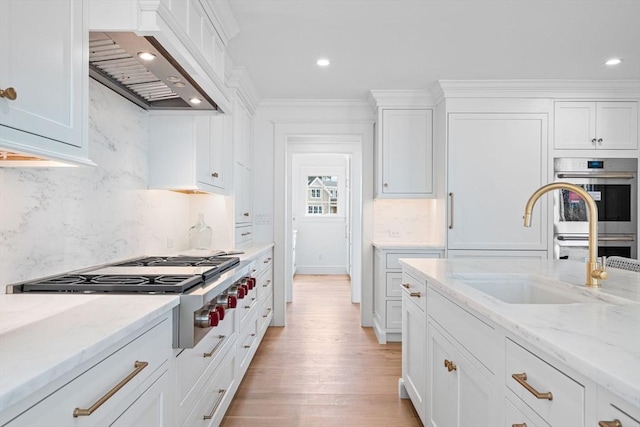 kitchen with a sink, ornamental molding, stainless steel appliances, custom range hood, and white cabinets