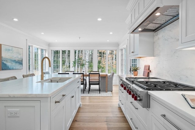 kitchen featuring a sink, light wood-style floors, stainless steel gas stovetop, crown molding, and wall chimney range hood