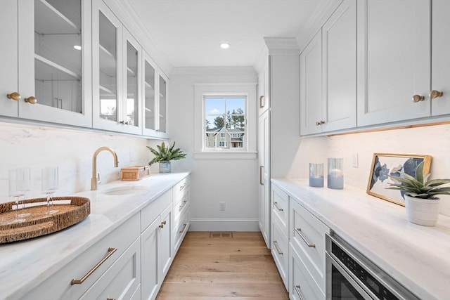 interior space featuring baseboards, light wood-type flooring, ornamental molding, recessed lighting, and a sink