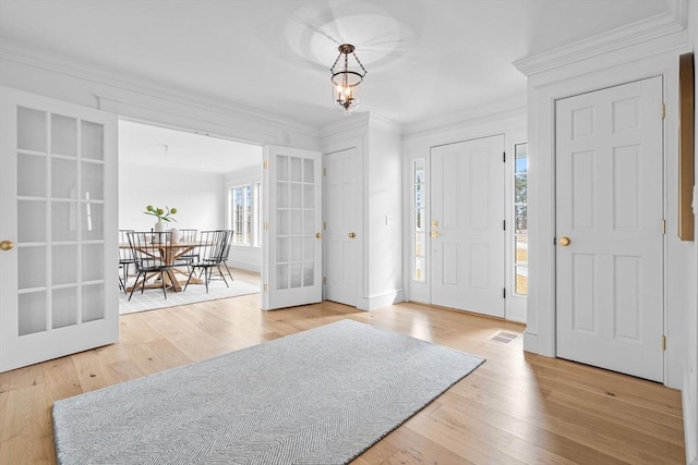 foyer entrance with french doors, wood finished floors, ornamental molding, and a chandelier