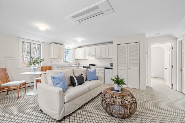 living area with visible vents, light carpet, a wainscoted wall, a baseboard heating unit, and vaulted ceiling