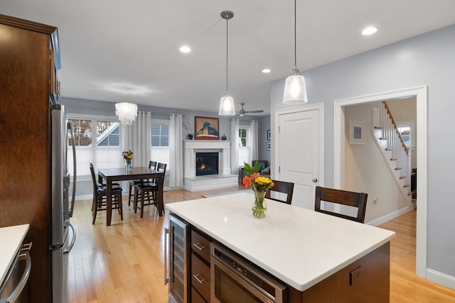 kitchen featuring appliances with stainless steel finishes, ceiling fan with notable chandelier, beverage cooler, light hardwood / wood-style floors, and a kitchen island