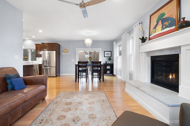 living room featuring ceiling fan, a fireplace, and light wood-type flooring