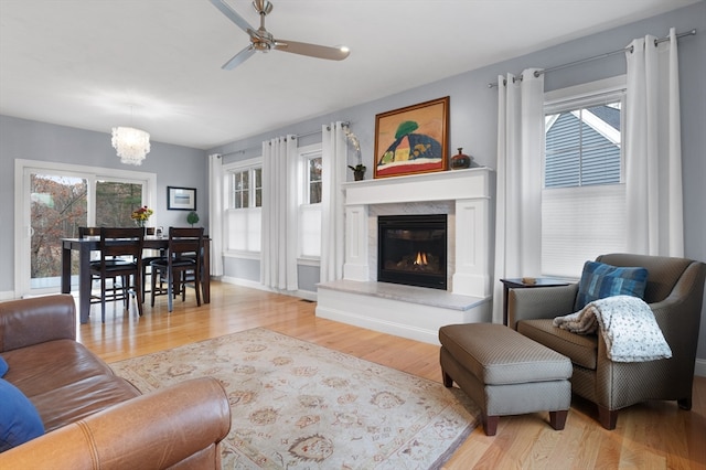 living room featuring ceiling fan with notable chandelier, light hardwood / wood-style floors, and a premium fireplace