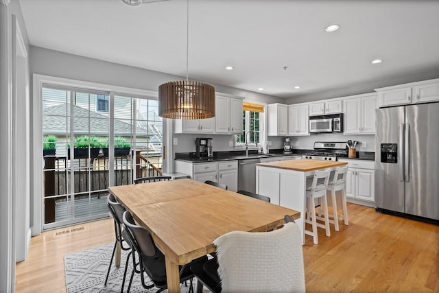 kitchen featuring appliances with stainless steel finishes, white cabinetry, light wood-type flooring, sink, and pendant lighting