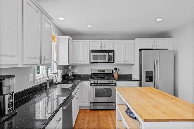 kitchen featuring light wood-type flooring, white cabinets, dark stone countertops, and stainless steel appliances