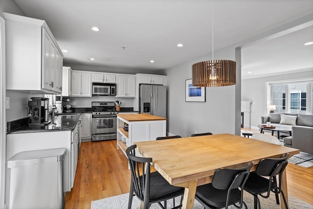 kitchen with appliances with stainless steel finishes, wooden counters, white cabinets, light wood-type flooring, and pendant lighting