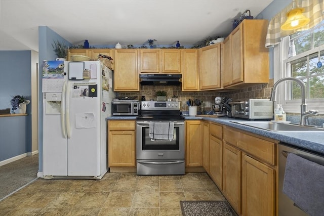 kitchen with appliances with stainless steel finishes, a sink, under cabinet range hood, tasteful backsplash, and baseboards