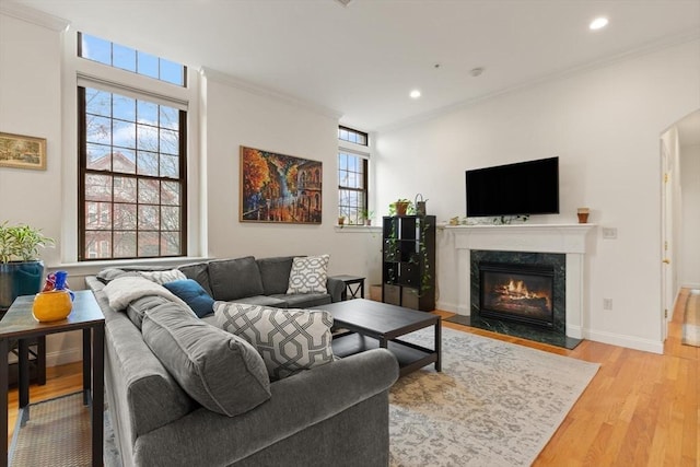 living area featuring ornamental molding, recessed lighting, a high end fireplace, arched walkways, and light wood-style flooring