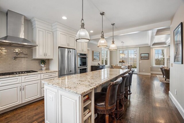 kitchen with a center island, decorative light fixtures, appliances with stainless steel finishes, white cabinets, and wall chimney range hood