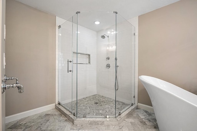 bathroom with marble finish floor, a freestanding bath, a shower stall, and baseboards