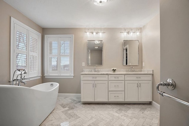 bathroom with double vanity, a freestanding tub, baseboards, and a sink