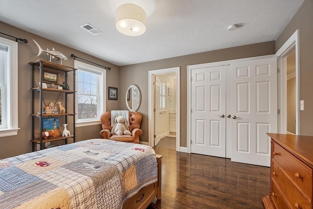 bedroom featuring a closet, visible vents, ensuite bathroom, dark wood-type flooring, and baseboards