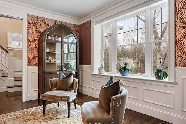 sitting room featuring a decorative wall, dark wood-type flooring, ornamental molding, stairway, and wainscoting