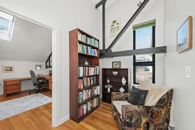 living area with light wood-style floors, a skylight, built in study area, and high vaulted ceiling