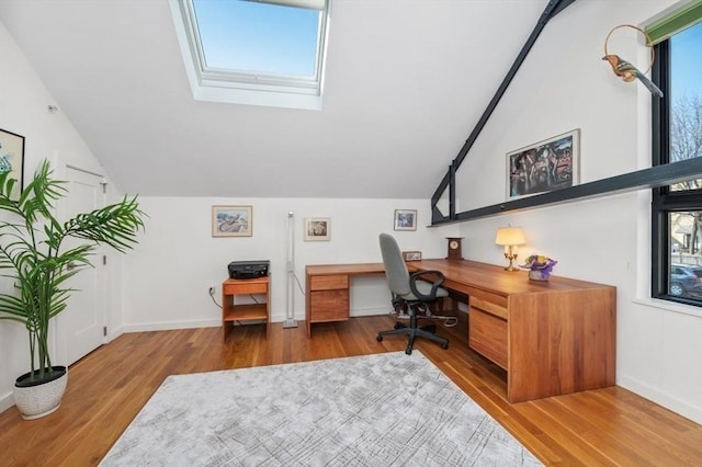 home office featuring vaulted ceiling with skylight, built in study area, baseboards, and wood finished floors