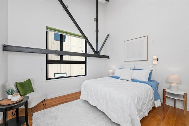 bedroom with a towering ceiling, baseboards, and wood finished floors