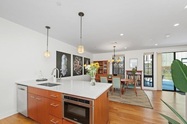 kitchen with light wood-style flooring, a sink, light countertops, stainless steel dishwasher, and brown cabinetry