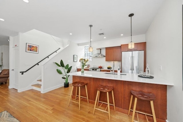 kitchen featuring a peninsula, stainless steel appliances, light countertops, wall chimney range hood, and a kitchen bar