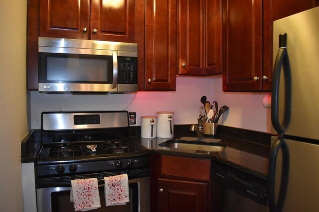 kitchen with appliances with stainless steel finishes, dark stone counters, and a sink