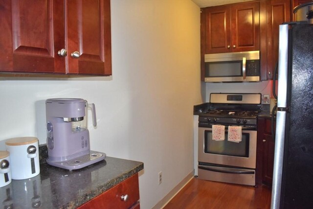 kitchen featuring dark stone counters, dark wood-style floors, baseboards, and appliances with stainless steel finishes