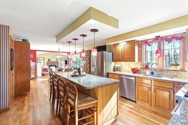 kitchen with a breakfast bar, a sink, light stone counters, stainless steel appliances, and a fireplace