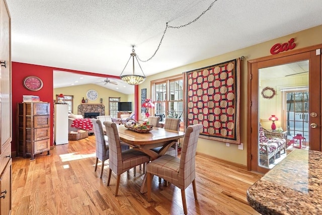 dining room featuring a stone fireplace, vaulted ceiling, a textured ceiling, light wood-type flooring, and a chandelier