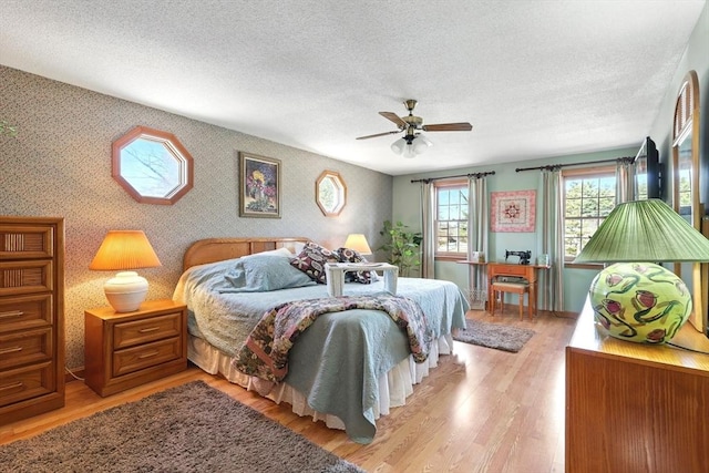 bedroom featuring a textured ceiling, wallpapered walls, light wood-style floors, and a ceiling fan