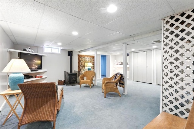 carpeted living area with a drop ceiling and a wood stove