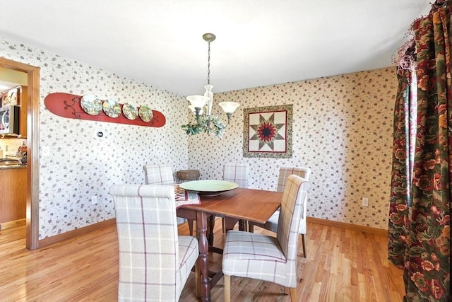 dining area featuring light wood finished floors, an inviting chandelier, wallpapered walls, and baseboards