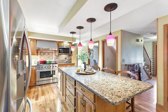 kitchen featuring stainless steel appliances, light wood finished floors, a breakfast bar area, and wall chimney range hood