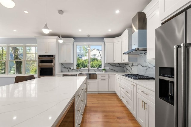 kitchen with wall chimney range hood, appliances with stainless steel finishes, light stone counters, a sink, and decorative backsplash